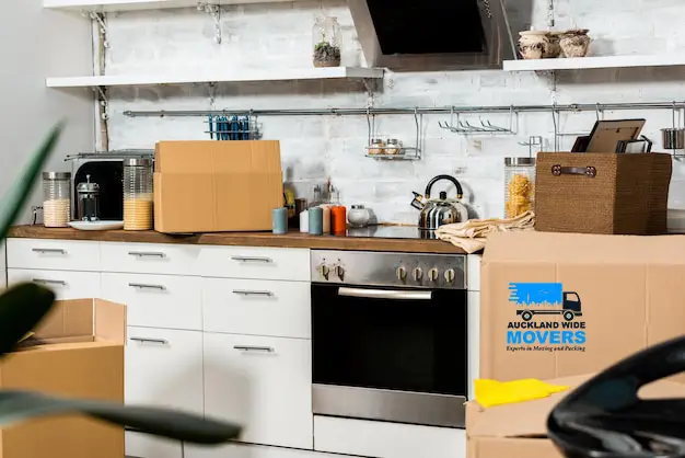 Hands carefully wrapping a wine glass with packing paper and bubble wrap to protect fragile kitchen items during a move.