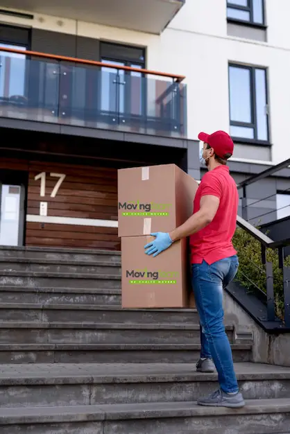 A mover placing protective padding in an apartment building's common area hallway to prevent damage during a move in Auckland.