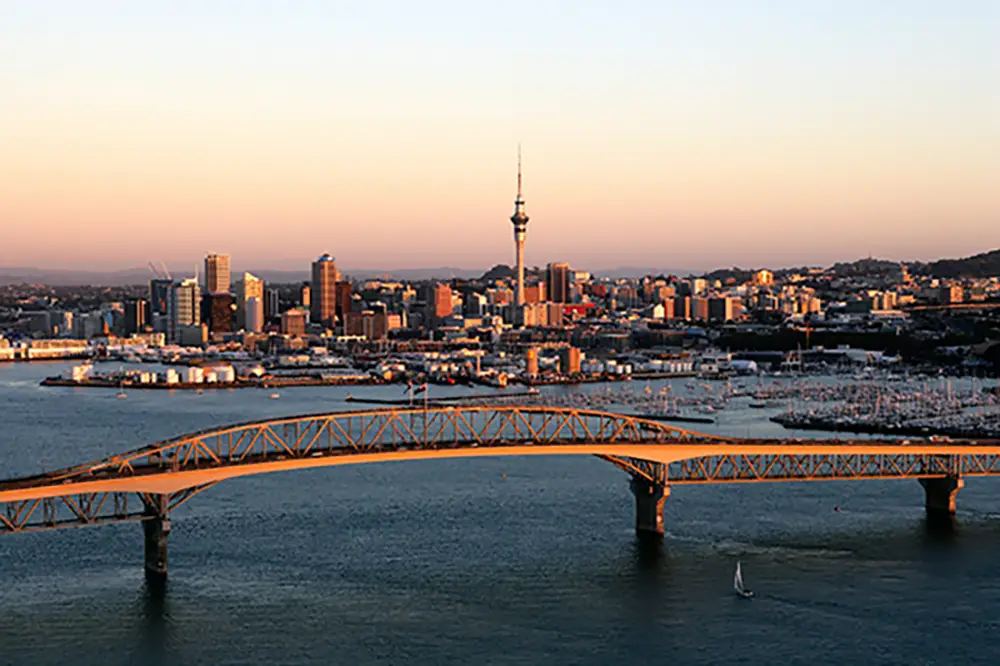 A moving truck driving with the Auckland Sky Tower and city skyline in the background, representing region-wide service.